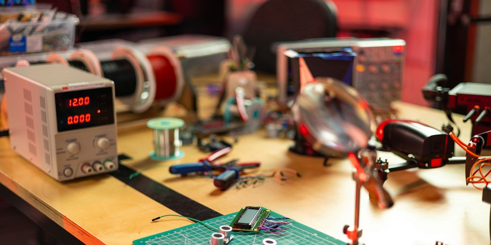 An electronics workbench with a bench power supply, a magnifier on a stand and a small quad frame.