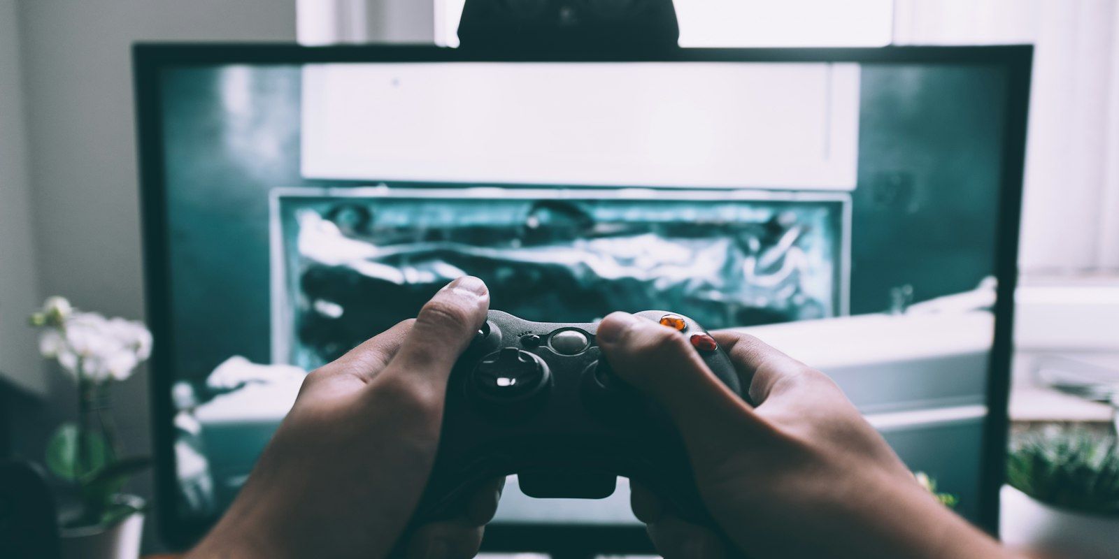 Two hands holding a game controller in front of a monitor.