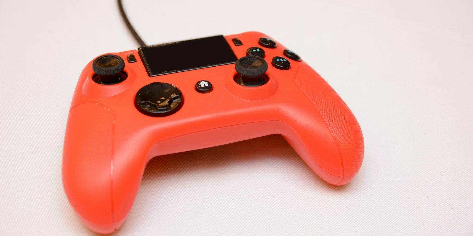 An orange wired game controller on a white table.